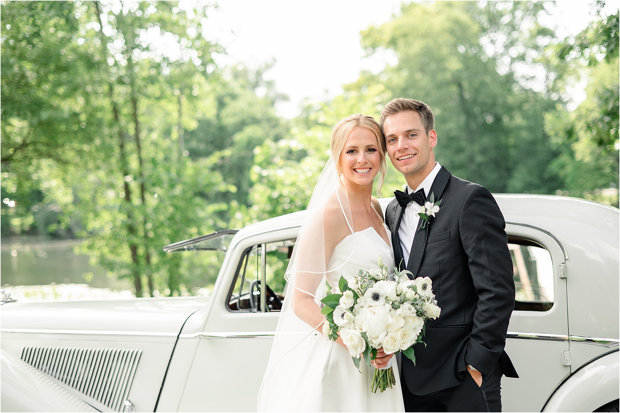 Emily and Ben on their wedding day standing next to their family's classic Jaguar car.